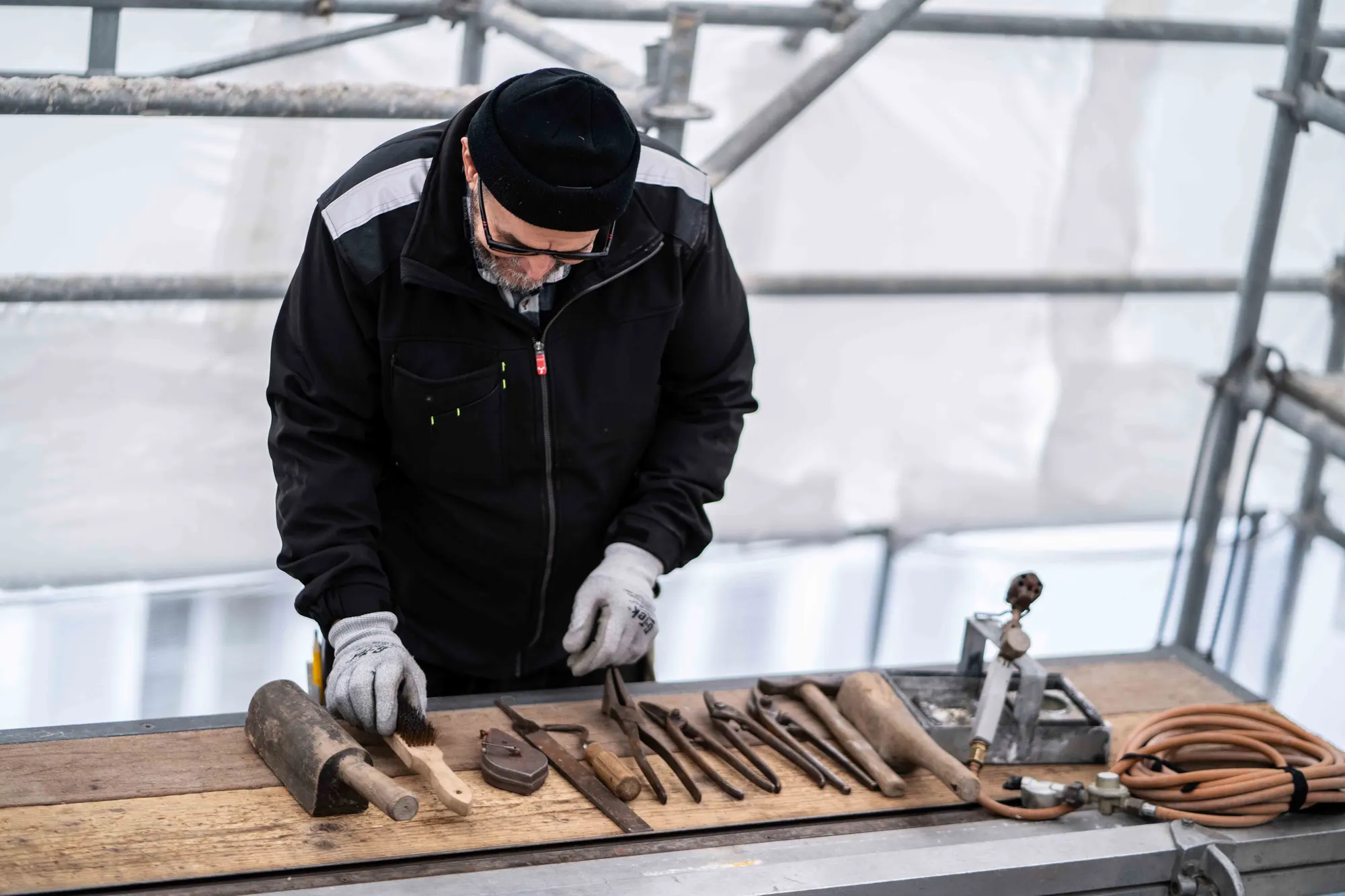 Couvreur préparant ses outils de zinguerie alignés sur un établi