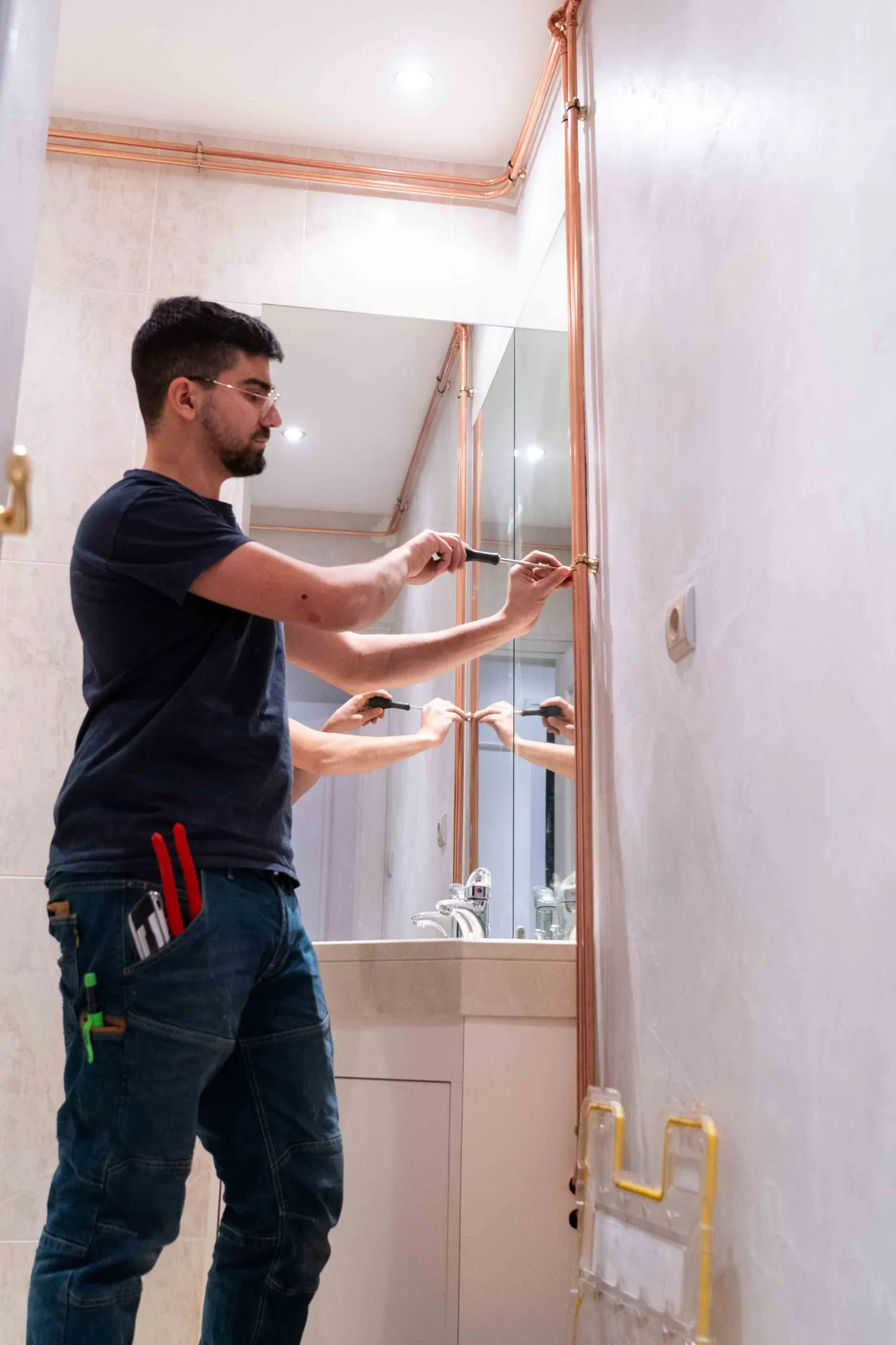 Plombier fixant une colonne en cuivre le long d'un mur de salle de bains